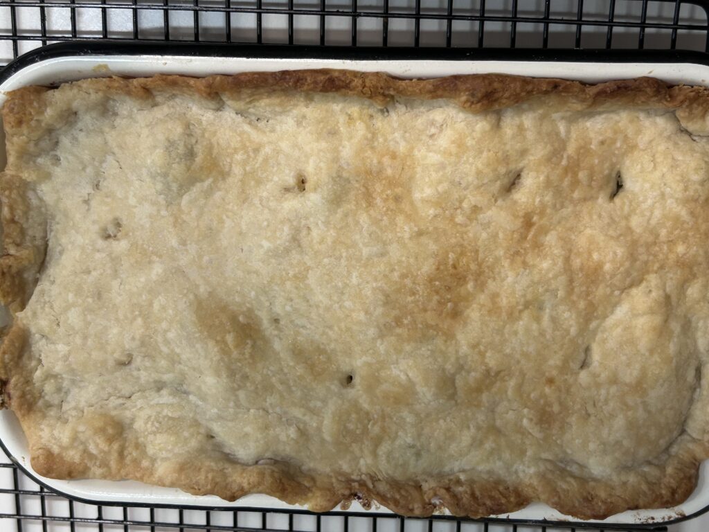 a freshly baked creamy chicken broccoli pie cooling on a black rack.