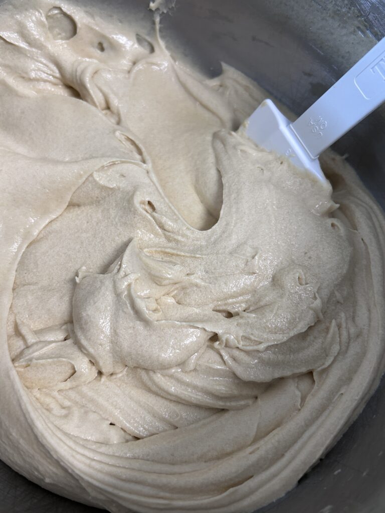 cake batter and a white plastic spatula in a metal mixing bowl. 