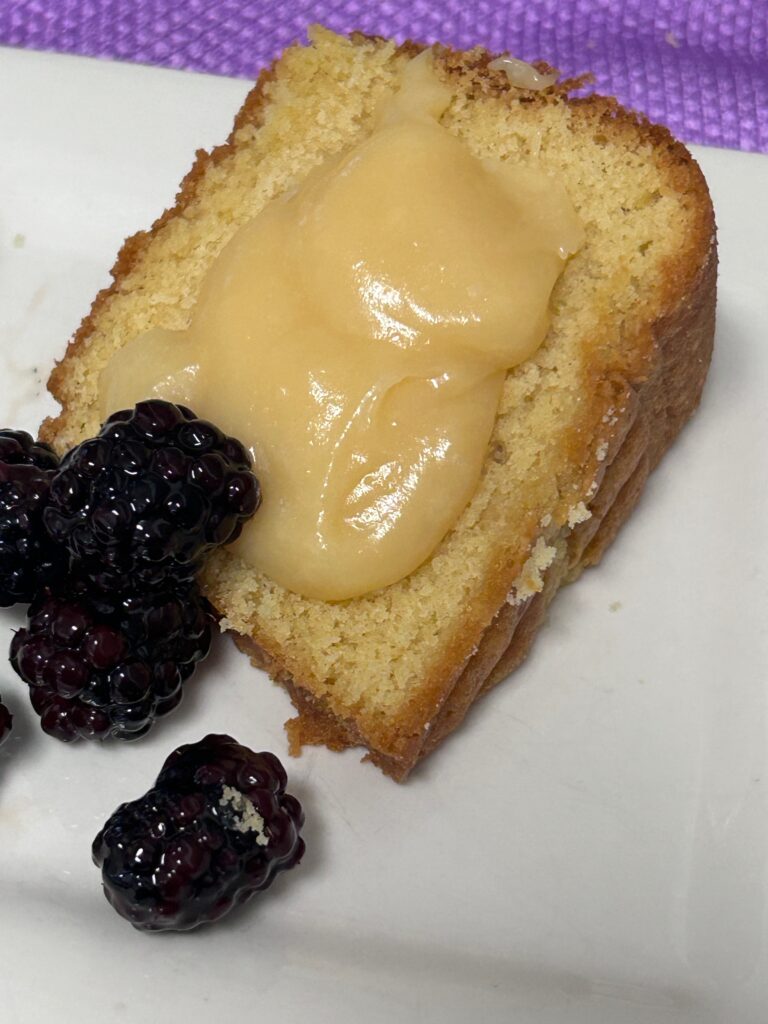 a slice of almond rum pound cake on a white plate with blackberries and lemon curd. 