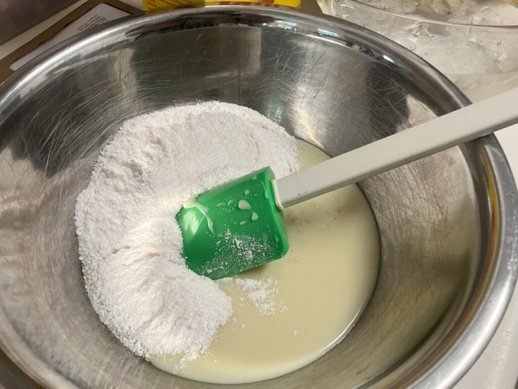 instant pudding mix being added to condensed milk in a metal bowl.