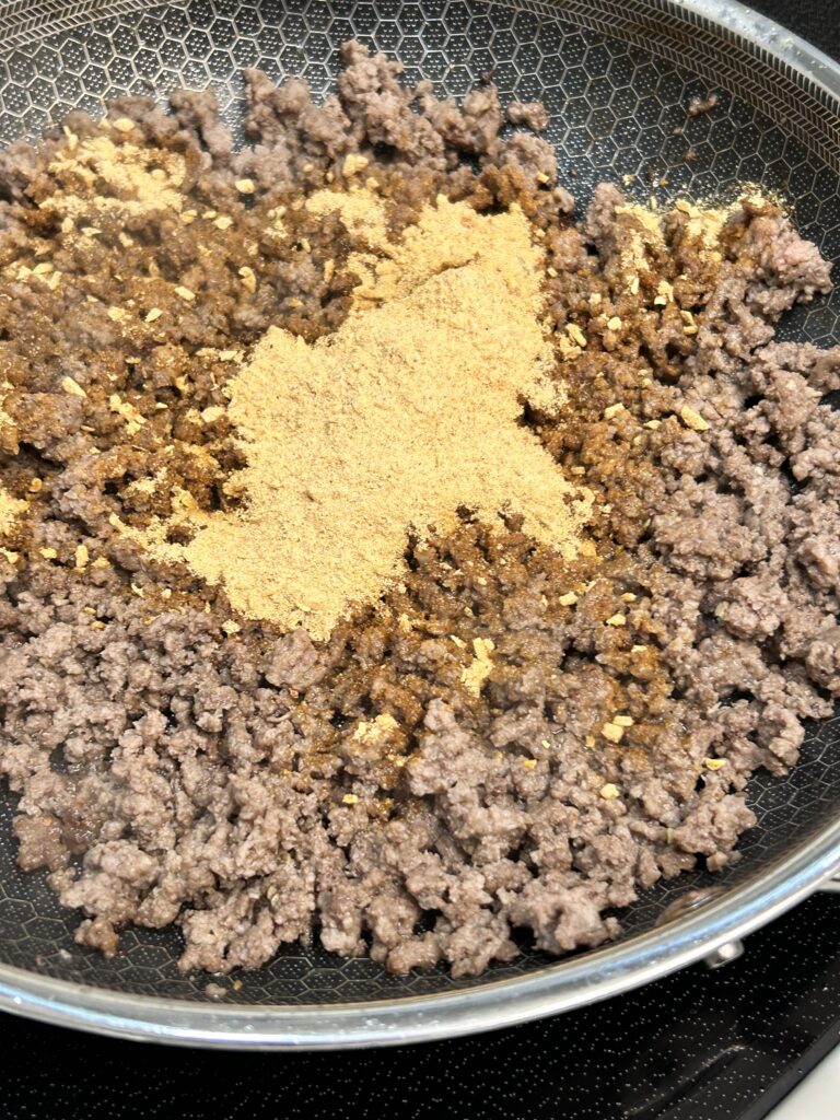 ground beef in a pan with sloppy joe seasoning being sprinkled over.