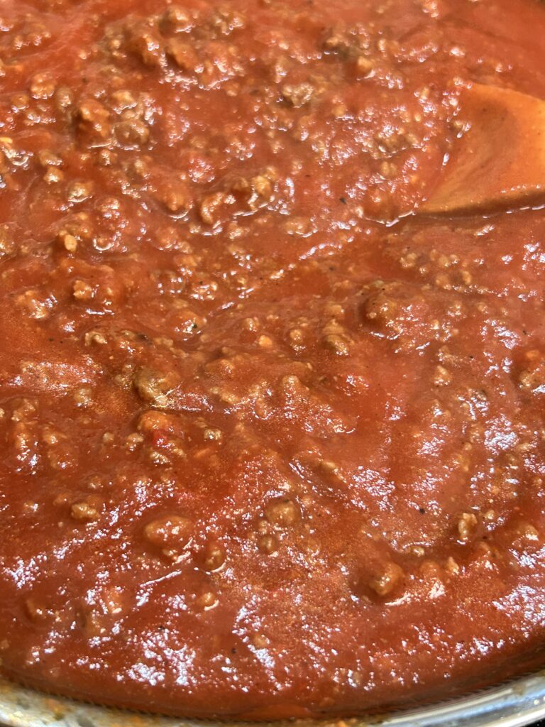 sloppy joe filling simmering in a saucepan with a wooden spoon.