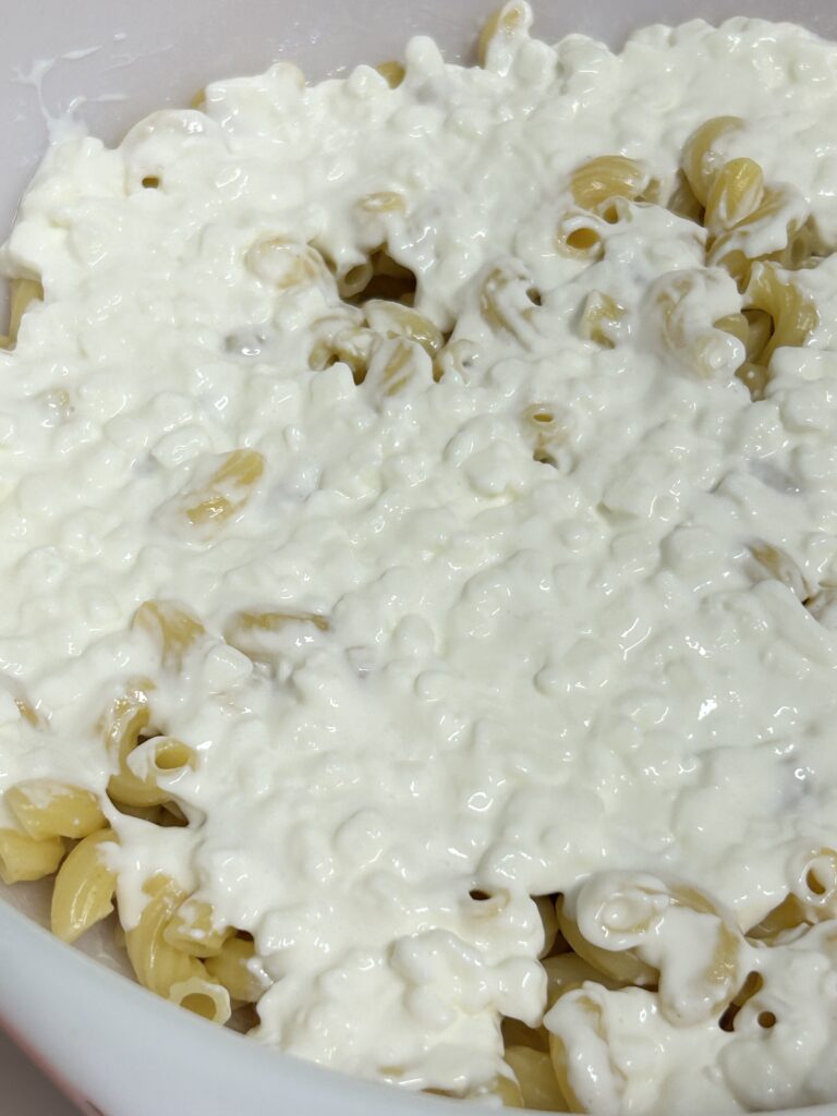 cooked pasta in a casserole dish being topped with cottage cheese.