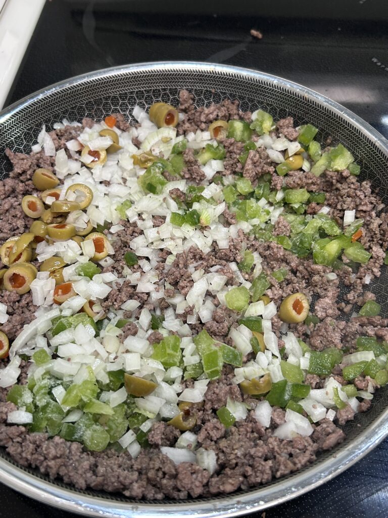ground beef, olives, onion and green bell pepper in a frying pan. 