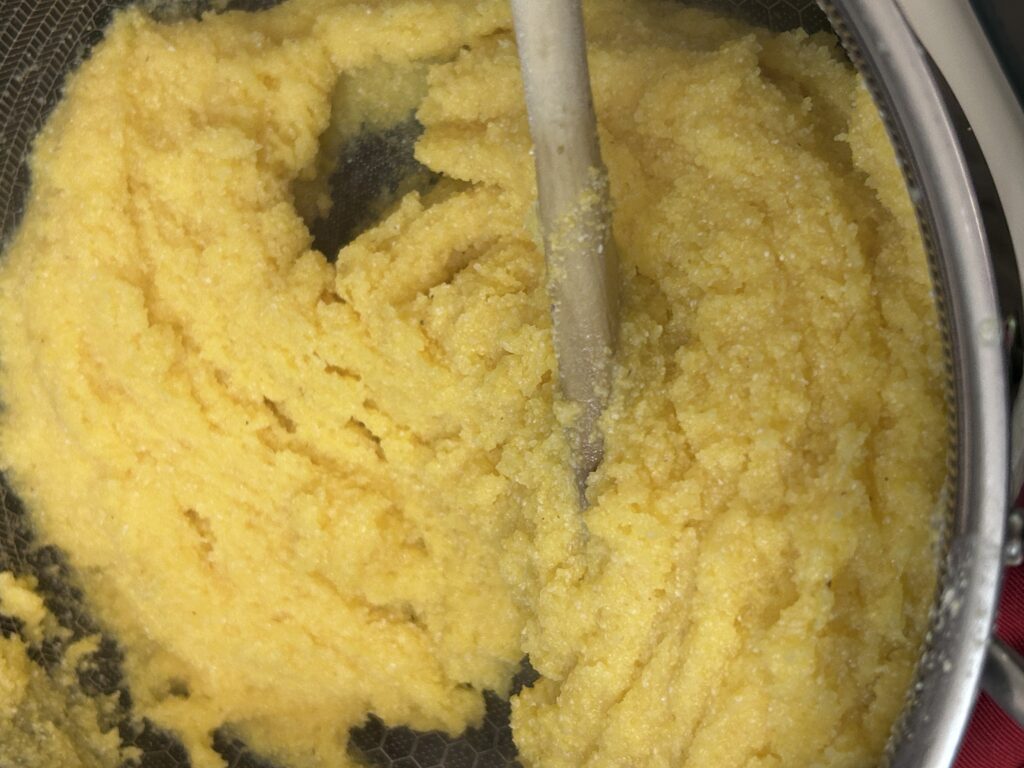 polenta being stirred with broth to thicken.