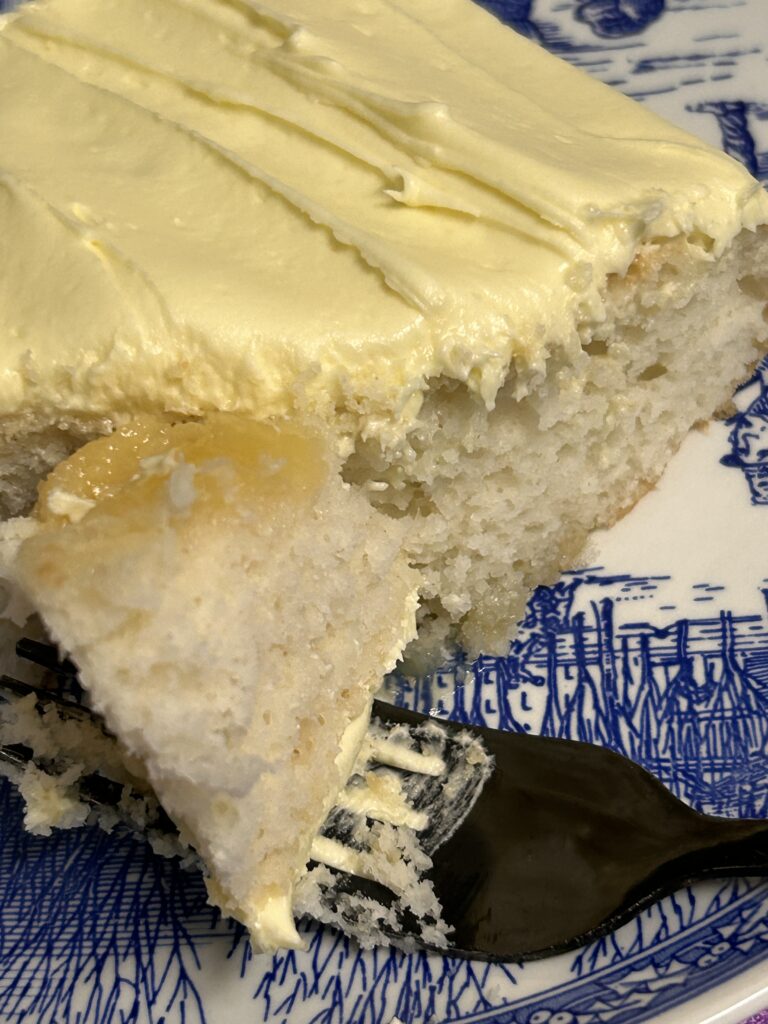a slice of homemade lemon love cake on a blue and white porcelain plate with a fork taking a bite.