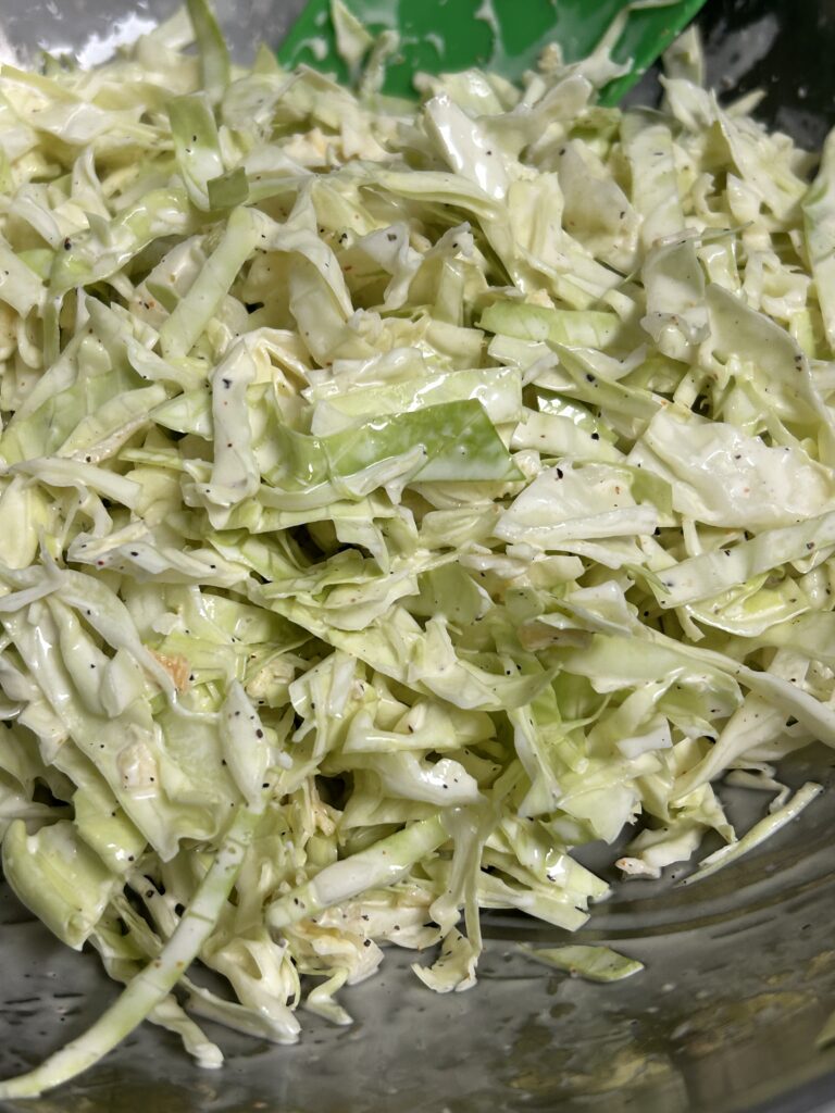 creamy coleslaw in a metal bowl with a green spatula.