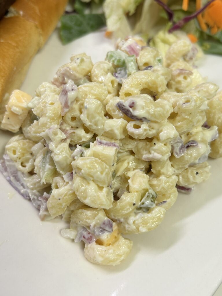 a serving of macaroni pasta salad with salami, pickles and cheese on a white plate.