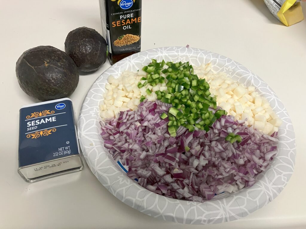 diced red onion, jicama and jalapeno on a plate with avocados and a bottle of sesame oil in the background.